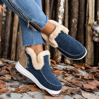 Navy blue textured slip-on trainers with cream plush trim and tan heel panels, worn with legs crossed against a log backdrop. 4
