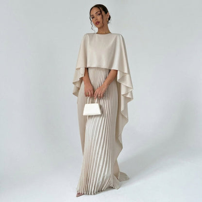 Model in the cream maxi dress with draped cape top and pleated skirt, holding a small white handbag 1