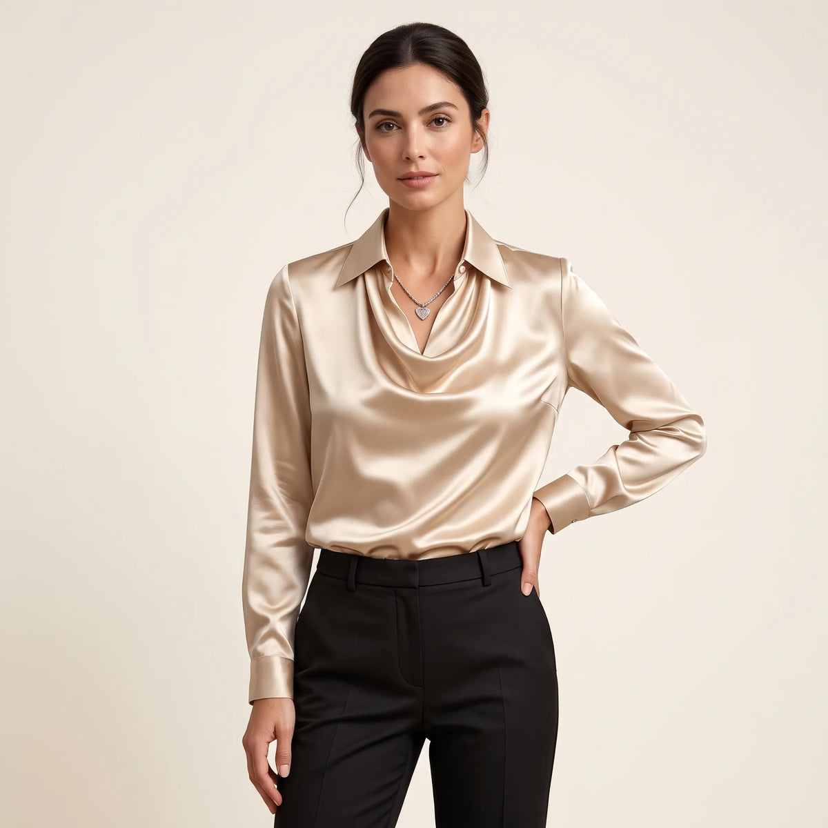 Model in a champagne satin blouse with draped collar, black trousers and heart pendant, hand on hip 12