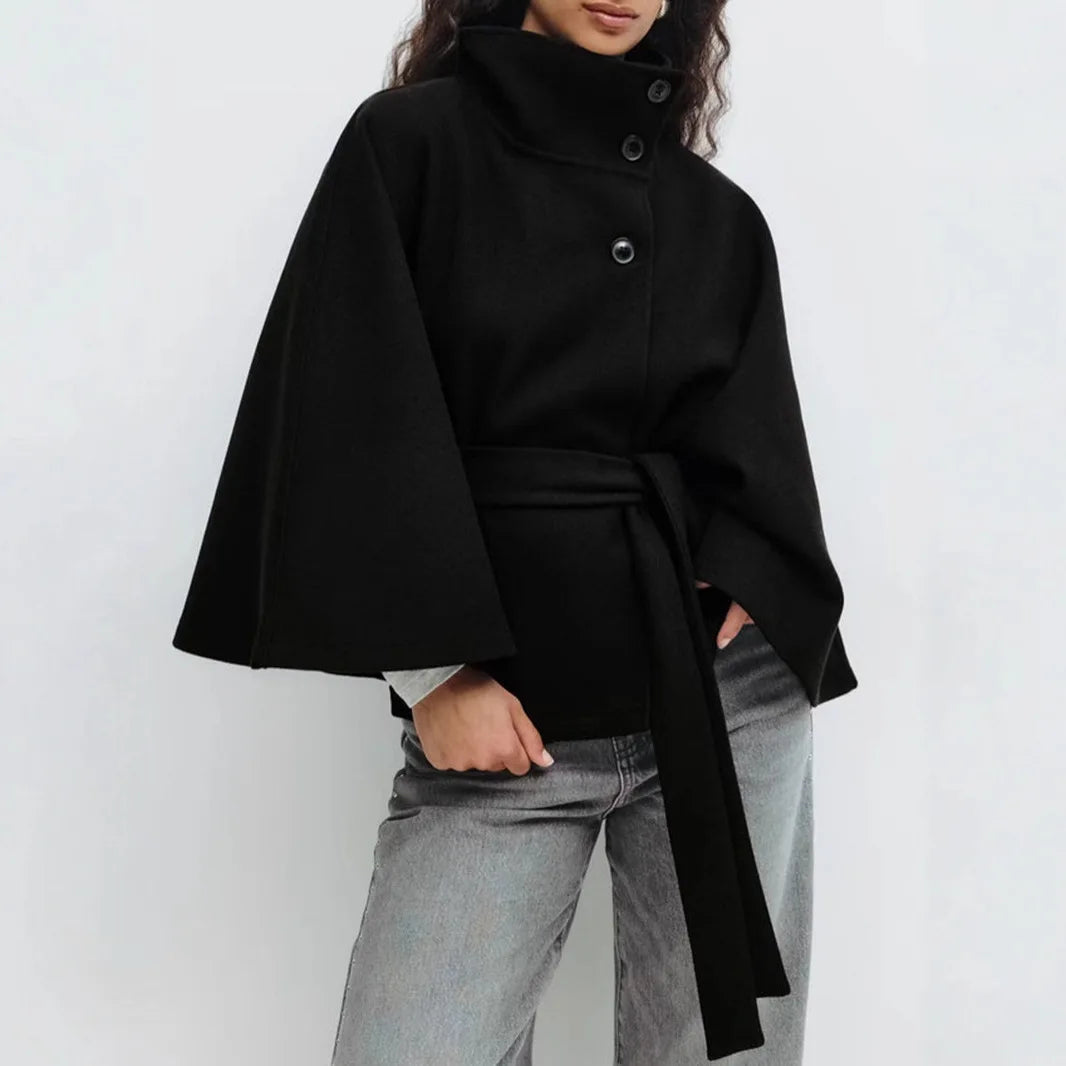 Black cape jacket worn with grey jeans, three buttons down the front and a long belt 12
