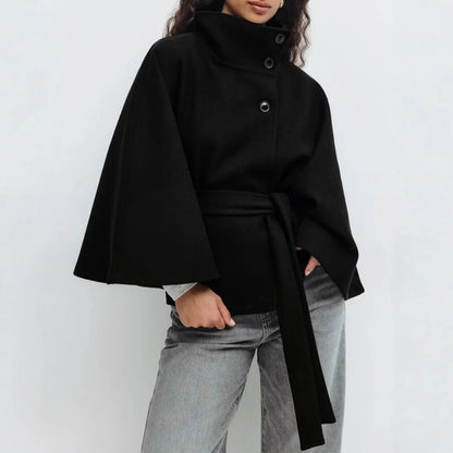 Black cape jacket worn with grey jeans, three buttons down the front and a long belt 12