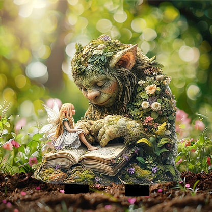 Moss-covered troll with a fairy reading on its open book, staked in dark soil with pink flowers behind. 10