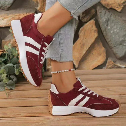 Burgundy trainers with white stripes and gum soles, side view of one raised shoe and one on wooden decking 13