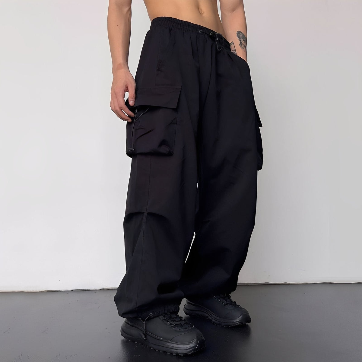 Model wears the baggy cargo trousers in black with black chunky trainers, side view 3