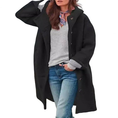 Black coat worn open over a grey top and scarf, hand in pocket, on a plain white background 14