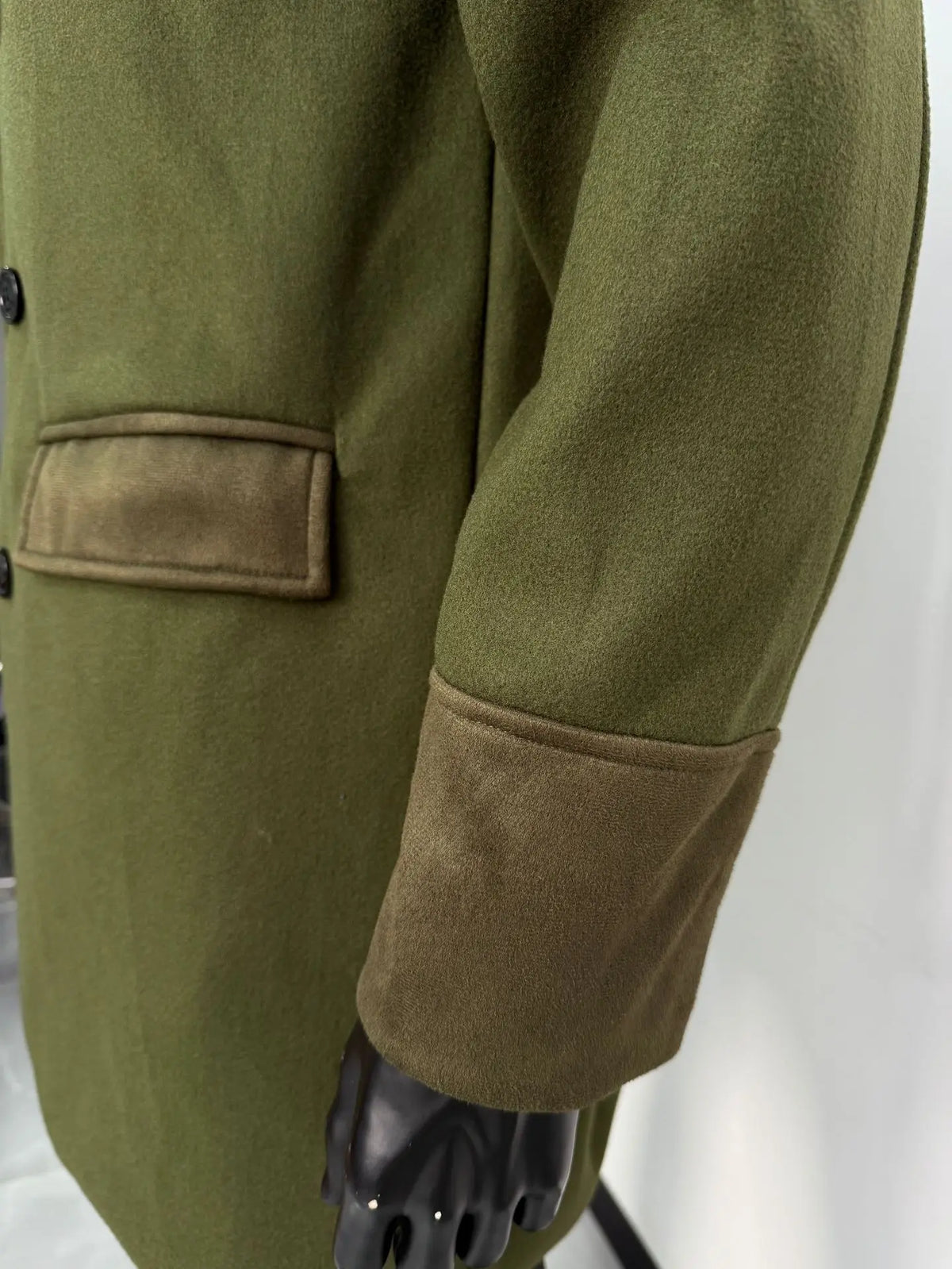 Close-up of the green coat's flap pocket and wide suede-look cuff on a mannequin's sleeve 15