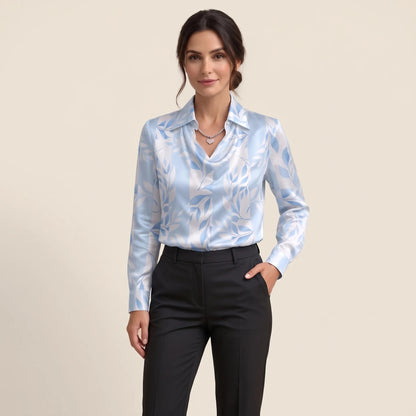 Model in a light blue and white leaf-print satin blouse with black trousers, one hand in pocket 15