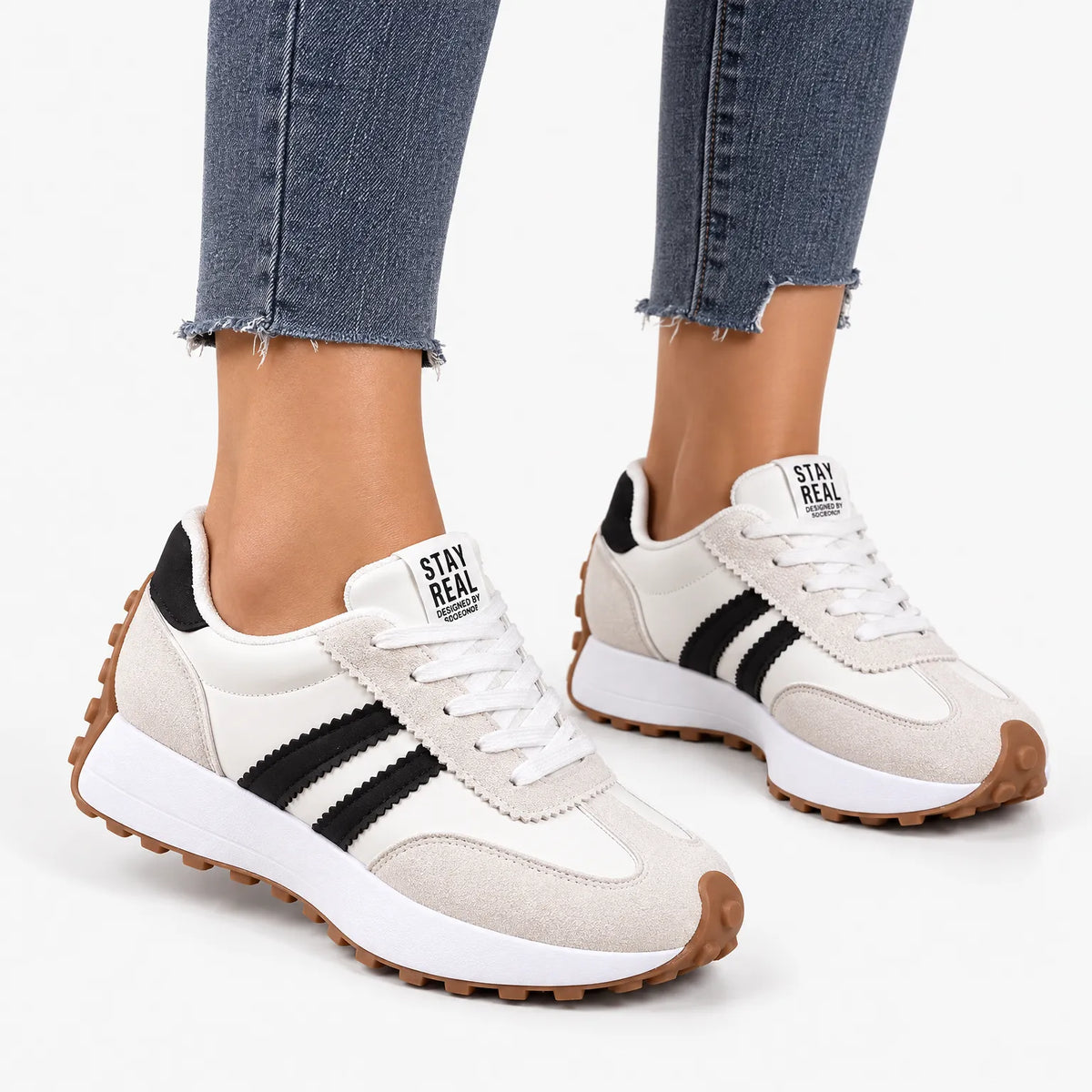 Cream suede and white trainers with black stripes and gum soles, worn with raw-hem jeans on a white background 15