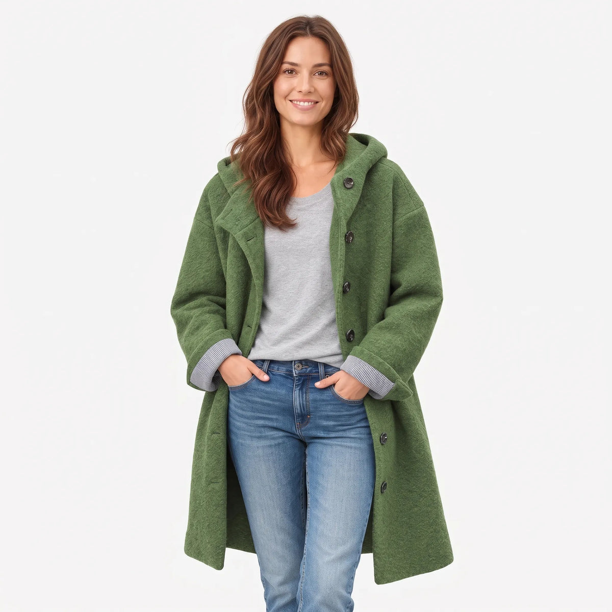 Full-length studio view of a model in the green coat, buttoned at the top, hands in jeans pockets 15