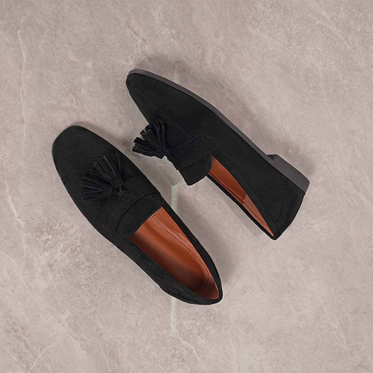 Flat lay of black tasselled loafers from above on marble, showing the tan insole 26