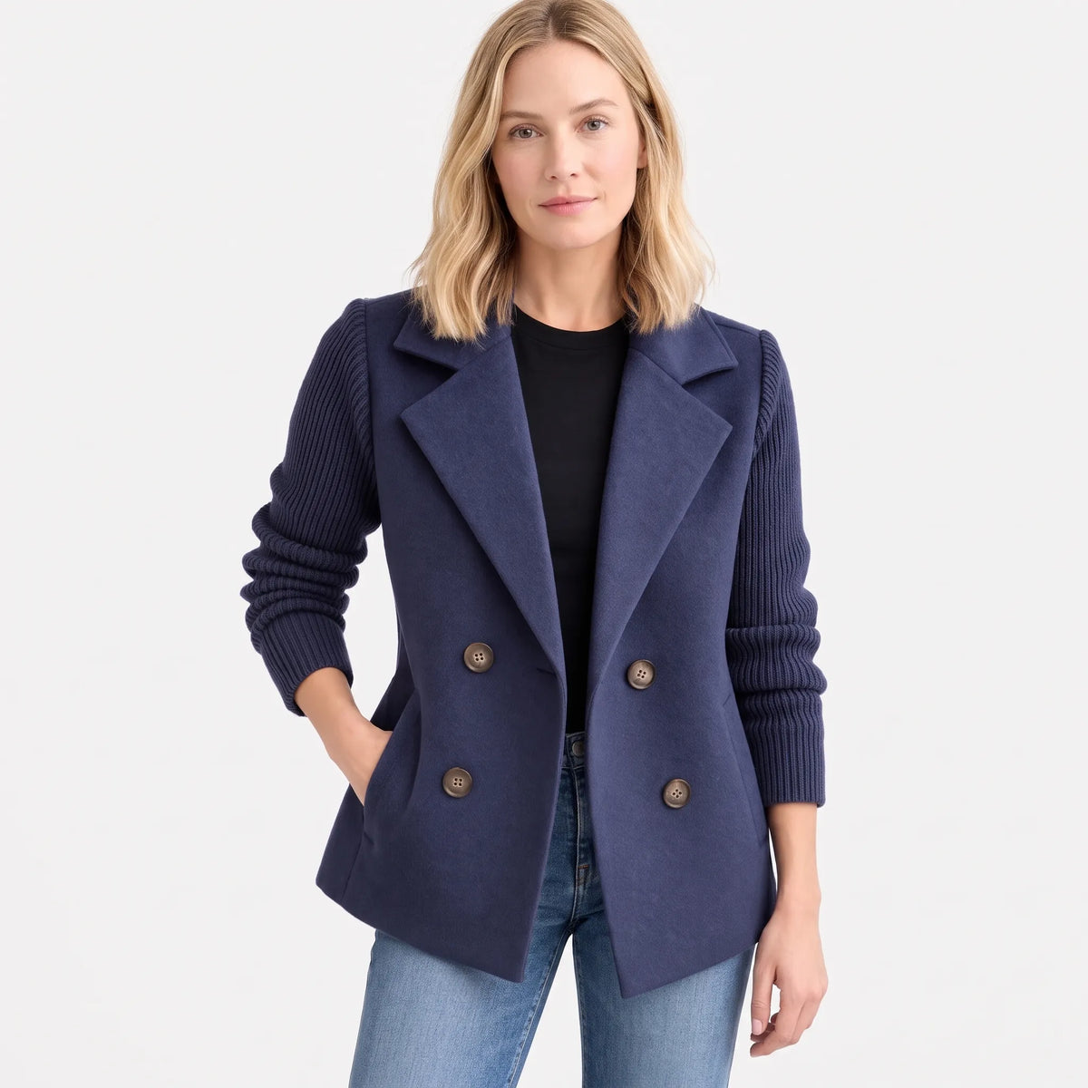 Navy double-breasted jacket with ribbed sleeves, model facing front with hand in pocket, plain white backdrop 16