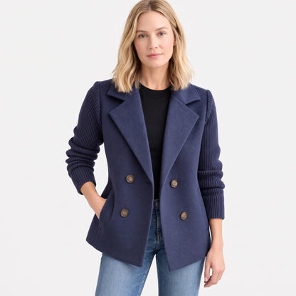 Navy double-breasted jacket with ribbed sleeves, model facing front with hand in pocket, plain white backdrop 16