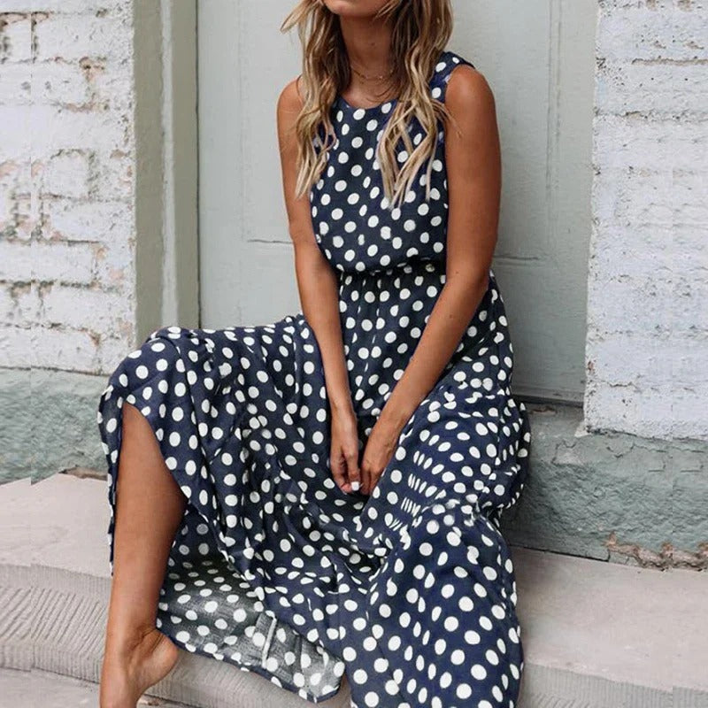 Woman sitting on a stone step wearing the navy blue polka dot dress, with its sleeveless top and loose flowing skirt. 5