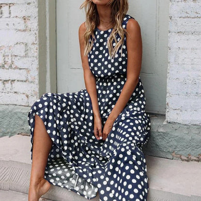 Woman sitting on a stone step wearing the navy blue polka dot dress, with its sleeveless top and loose flowing skirt. 5