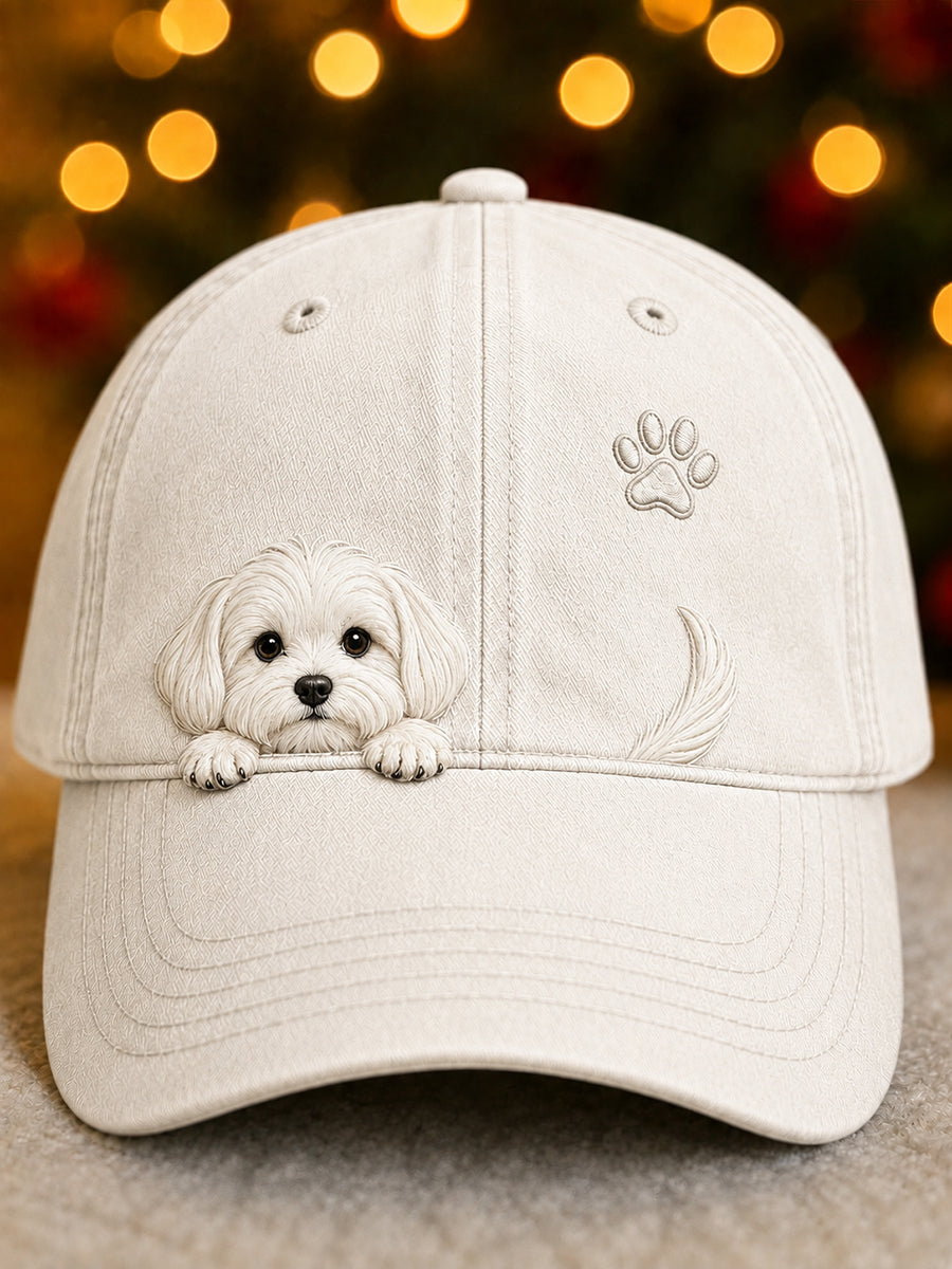Front view of the cap in off-white with an embossed peeking white puppy, paw print and tail, against softly glowing festive lights. 1
