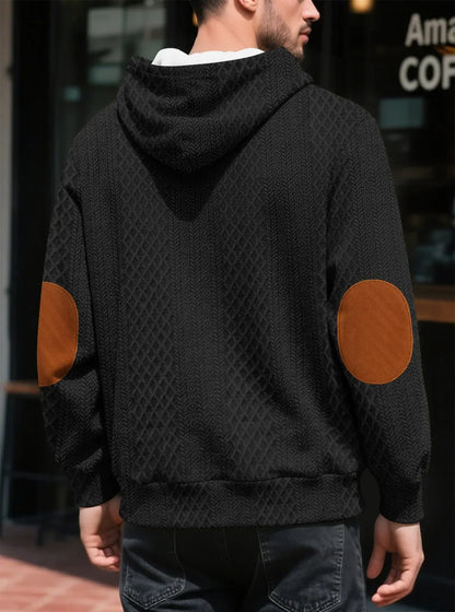 Back view of a black textured hoodie worn outdoors, showing large tan elbow patches and ribbed hem 17