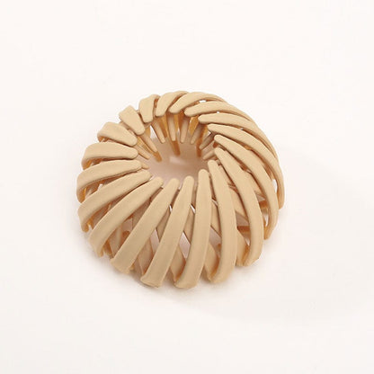 Single matte sand beige spiral clip with curved overlapping slats, photographed from above against a plain white background. 10