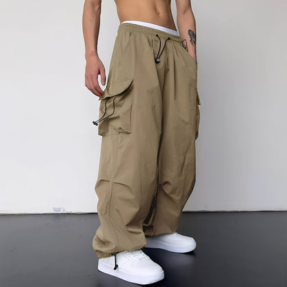 Model wears the baggy cargo trousers in sand beige with white trainers, side view 1