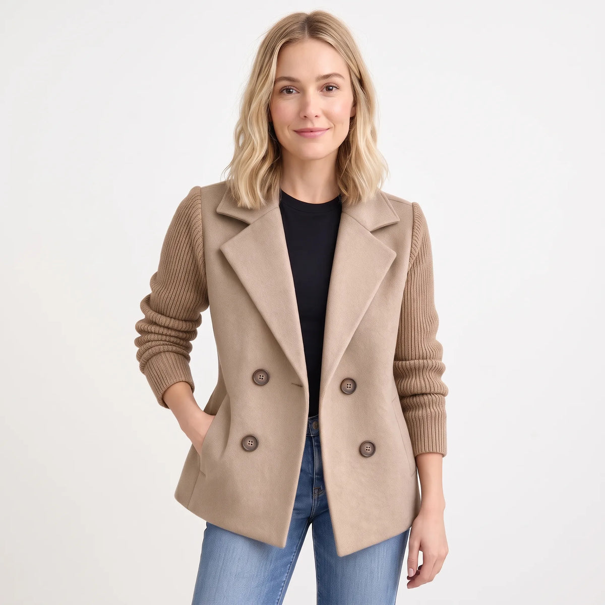 Studio shot of model in camel double-breasted jacket with ribbed knit sleeves, black top and jeans 18