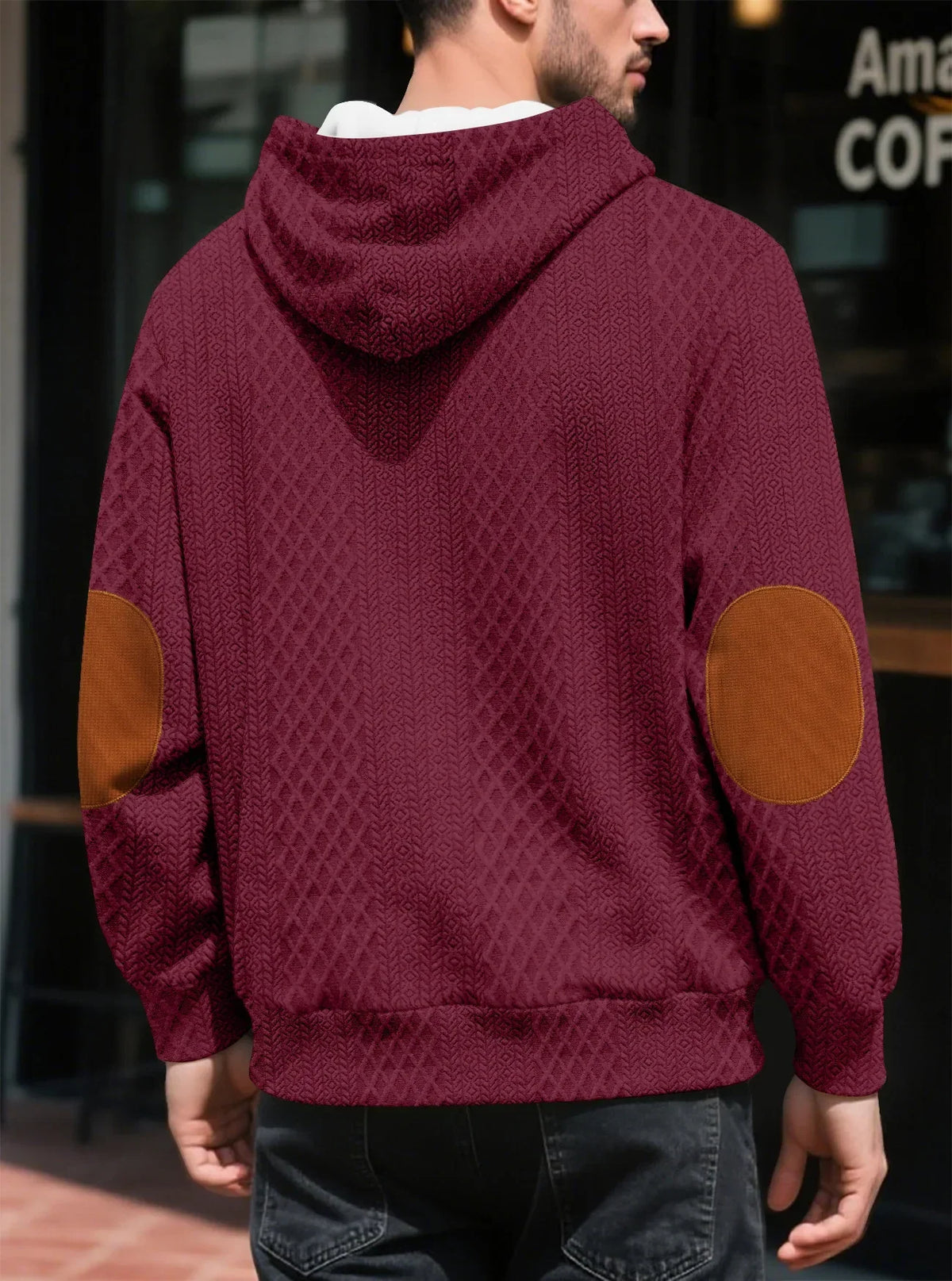 Back view of a burgundy textured hoodie on a model outdoors, showing tan elbow patches and the hood 19