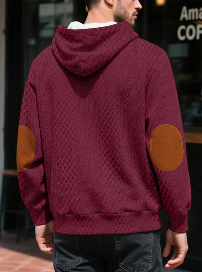 Back view of a burgundy textured hoodie on a model outdoors, showing tan elbow patches and the hood 19