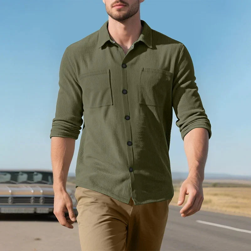 Model walking outdoors in the olive green ribbed shirt with sleeves rolled, under a blue sky 19