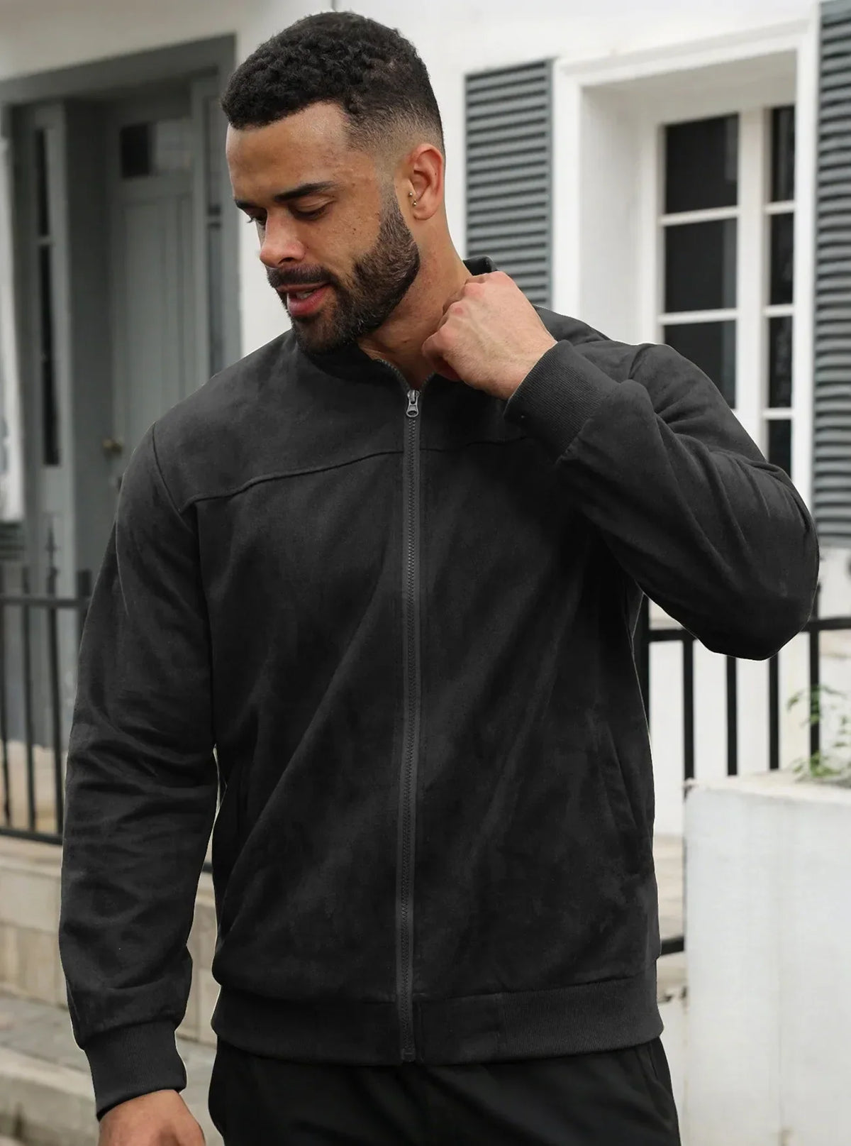 Bearded man outdoors in the black zip-up jacket, hand raised to his collar 19