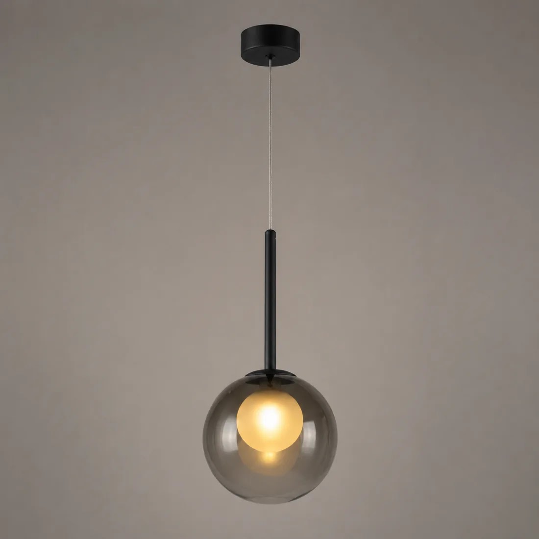Lit smoke grey globe pendant with black stem and ceiling plate against a taupe backdrop 10