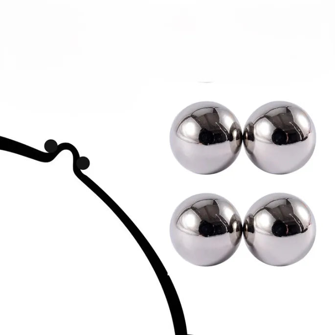 Two pairs of shiny silver magnetic balls beside a black line drawing of a bra strap or band for comparison. 6