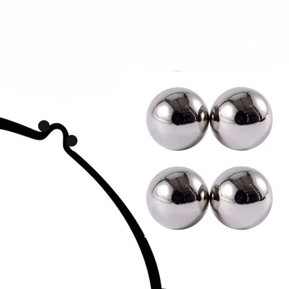 Two pairs of shiny silver magnetic balls beside a black line drawing of a bra strap or band for comparison. 6