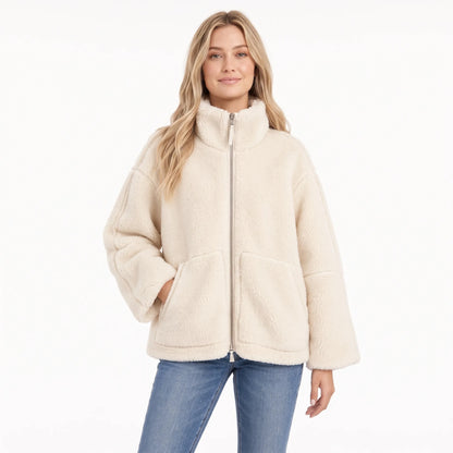 Woman in a cream fleece zip coat with large front pockets, one hand tucked in, with blue jeans 1