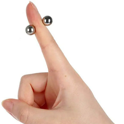 Hand pointing a finger upwards with two small silver magnetic balls attached either side of it, showing their size. 8