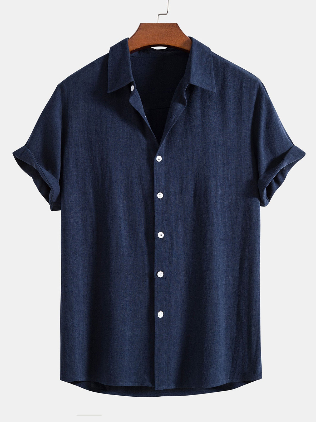 Short sleeve button-up shirt in navy blue on a wooden hanger, with turned-up sleeve cuffs and white buttons. 4