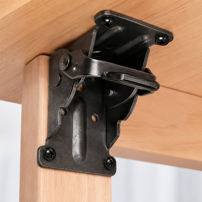 Close-up of a black steel bracket screwed under a wooden tabletop and down the leg, with its release lever visible. 2