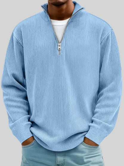 Man wearing the ribbed quarter-zip jumper in light blue over a white tee, hands in pockets of pale blue jeans. 1