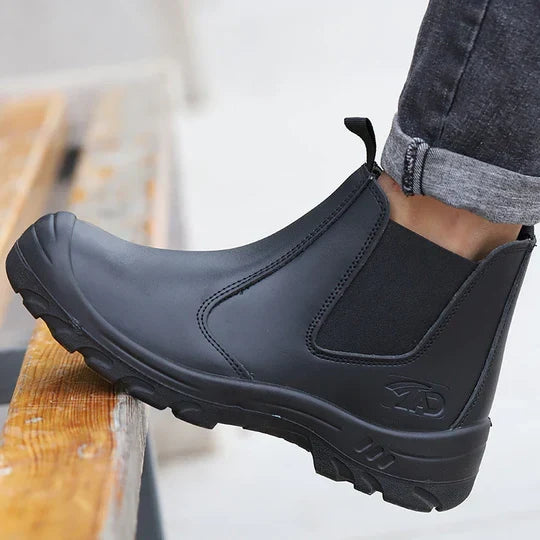 Side view of a black leather slip-on boot worn by a person with rolled grey jeans, foot resting on wooden steps 1