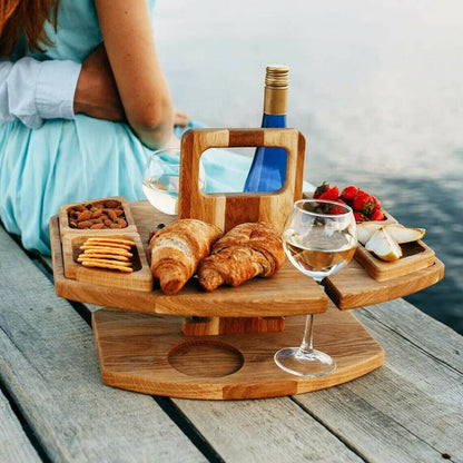 Wooden table with croissants, nuts, fruit, wine and glasses, set on a jetty beside a seated couple 2