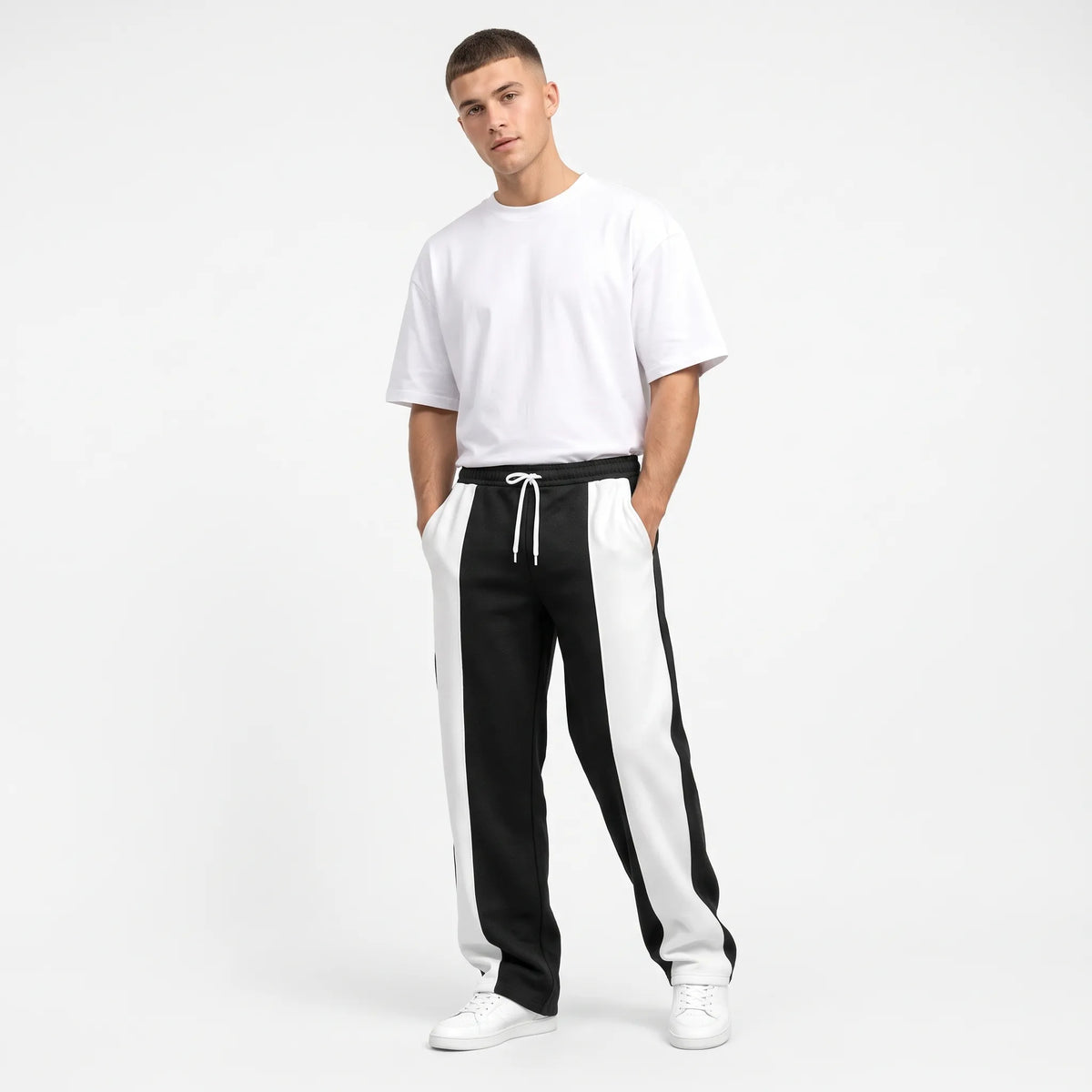 Model in black sweatpants with white side panels, white tee and trainers, hands in pockets 1