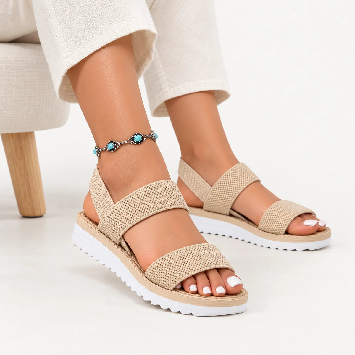 Beige woven elastic-strap sandals with white ridged soles, worn with cream trousers and a turquoise anklet 1
