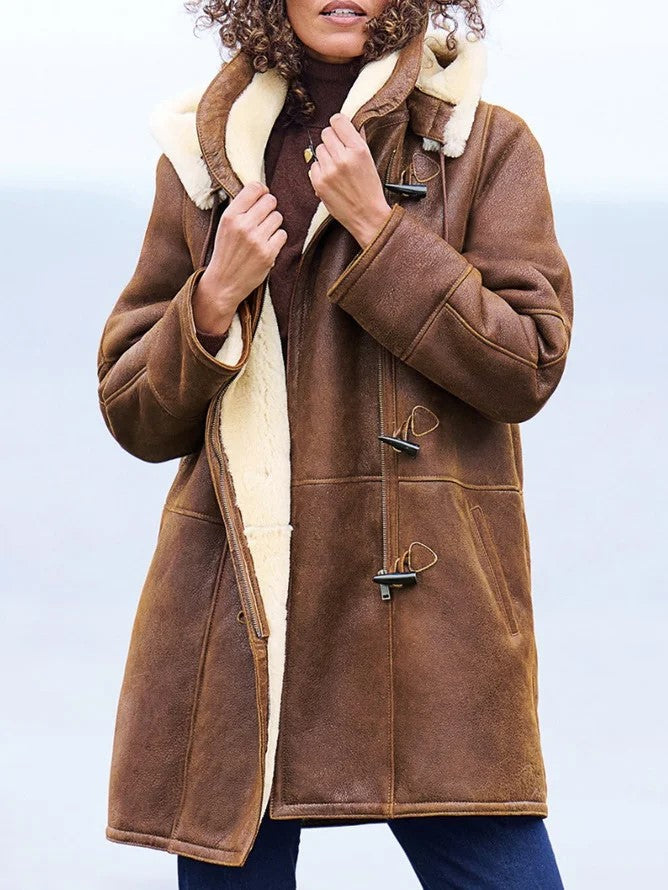 Woman wearing the brown coat open at the front, hands holding the cream fleece-lined collar, with toggle fastenings and front pockets visible. 1