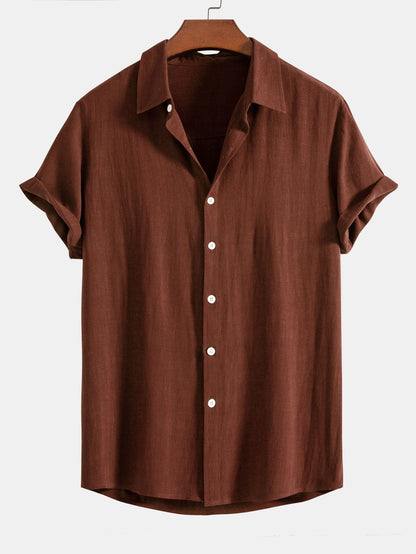 Short sleeve button-up shirt in rust brown on a wooden hanger, with cuffed sleeves and white buttons. 1