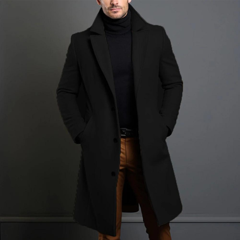 Model wearing the black longline single-breasted coat with notch lapels over a black roll-neck, hands in pockets, cropped at the chin. 1