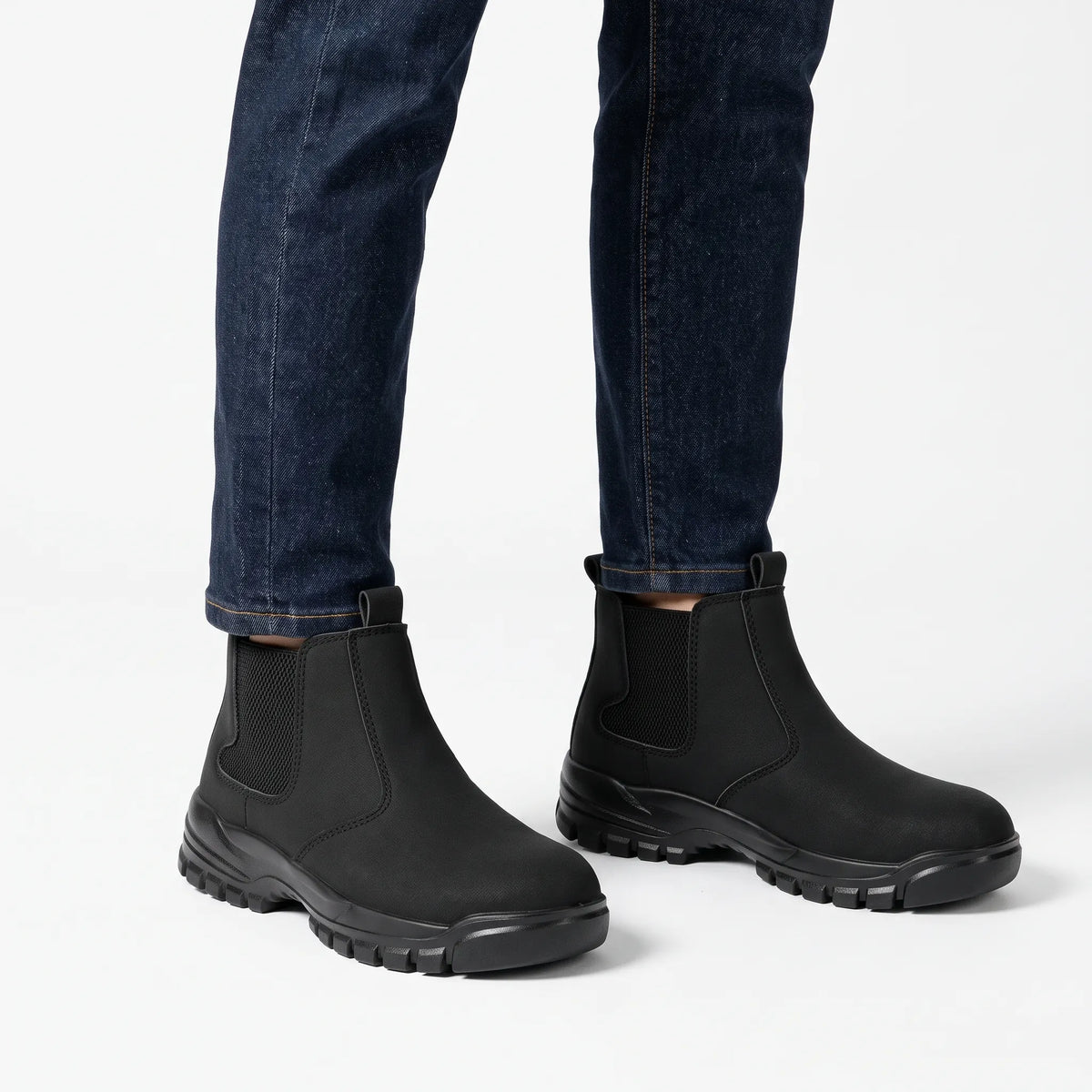 Black slip-on boots worn with dark indigo jeans against a plain white studio background 1