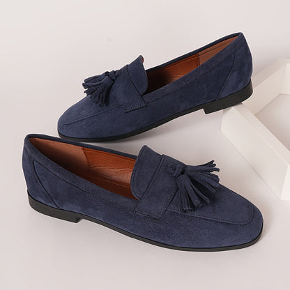 Pair of navy tasselled loafers on a white block, showing tan lining and low black heel 6