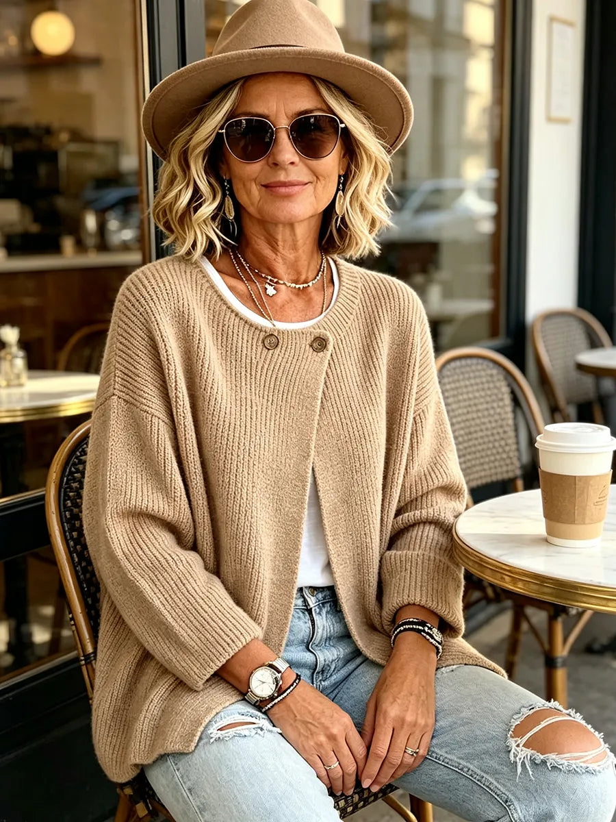 Model wearing the camel ribbed cardigan with a felt hat and sunglasses, seated outside a café 5