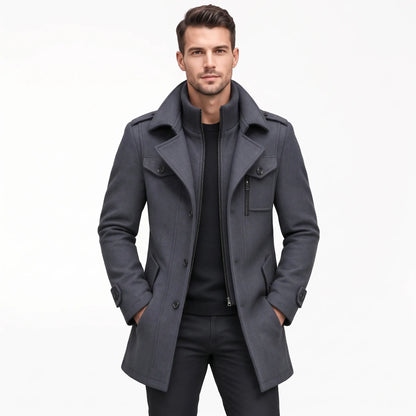 Man wearing the grey coat open over a black jumper and black trousers, hands in pockets 20