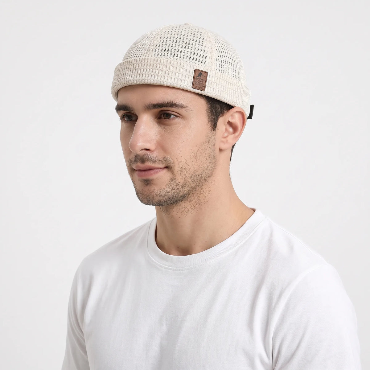 Man in a white t-shirt wearing the cream open weave brimless cap, seen from the front-left 22