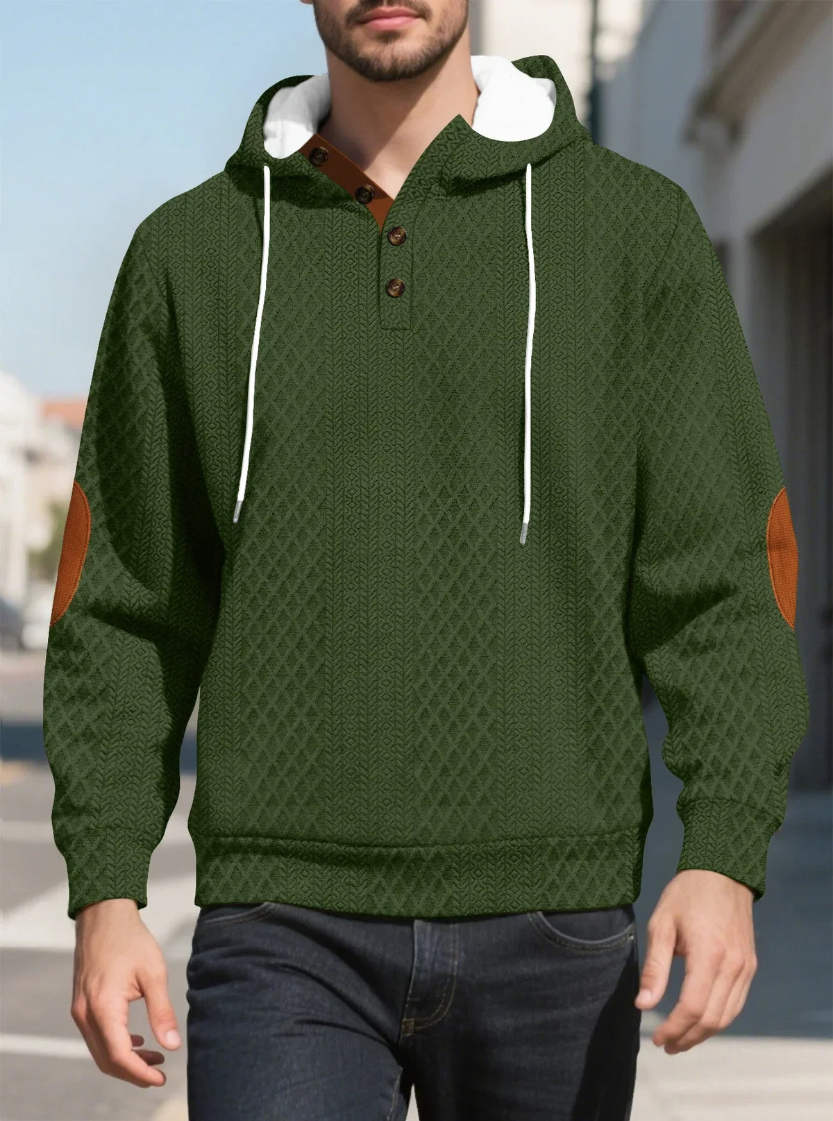 Olive green diamond-textured hoodie worn by a model walking outdoors, front view with tan elbow patches 22