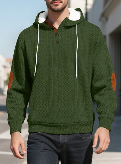 Olive green diamond-textured hoodie worn by a model walking outdoors, front view with tan elbow patches 22