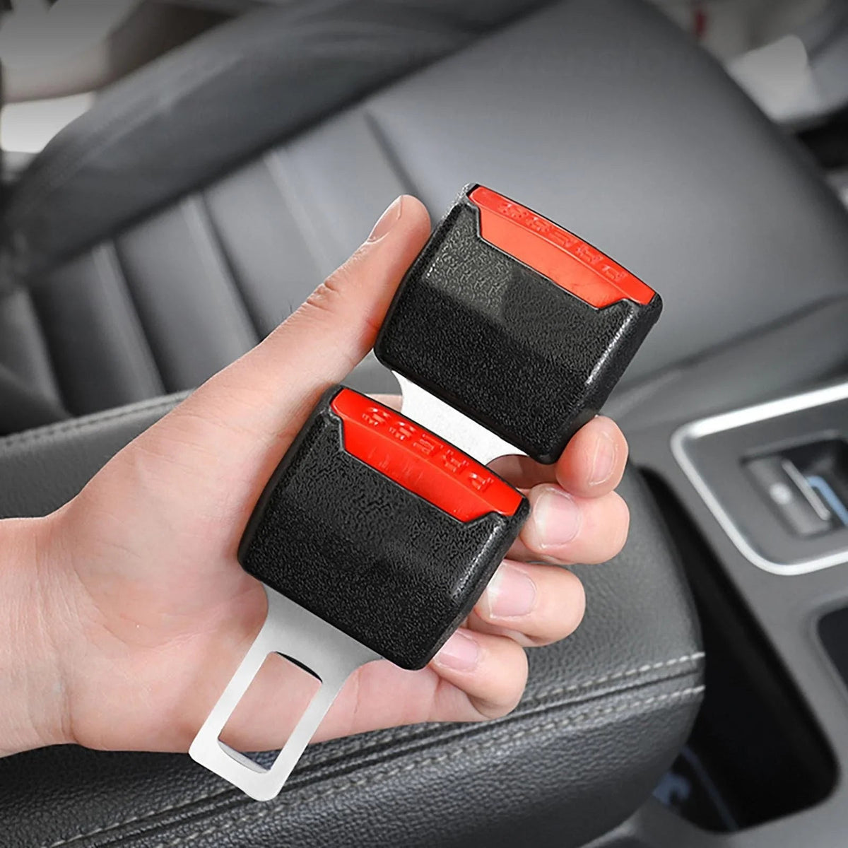 A hand holds both black and red buckle inserts, metal tongues pointing down, in a car interior 2